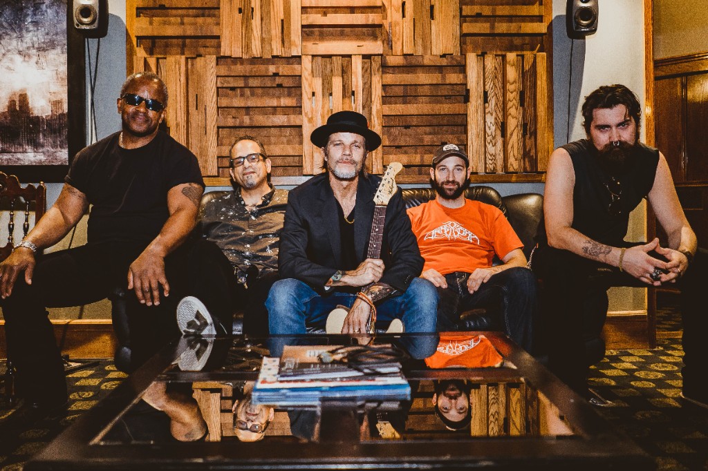 Black Electric, studio portrait 2019 — the five-piece seated in front of the wood-slat diffusers, Vitali center with the Telecaster